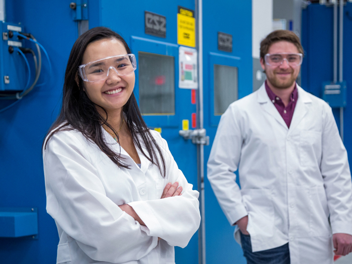 Woman and man in lab coat and safety glasses smiling