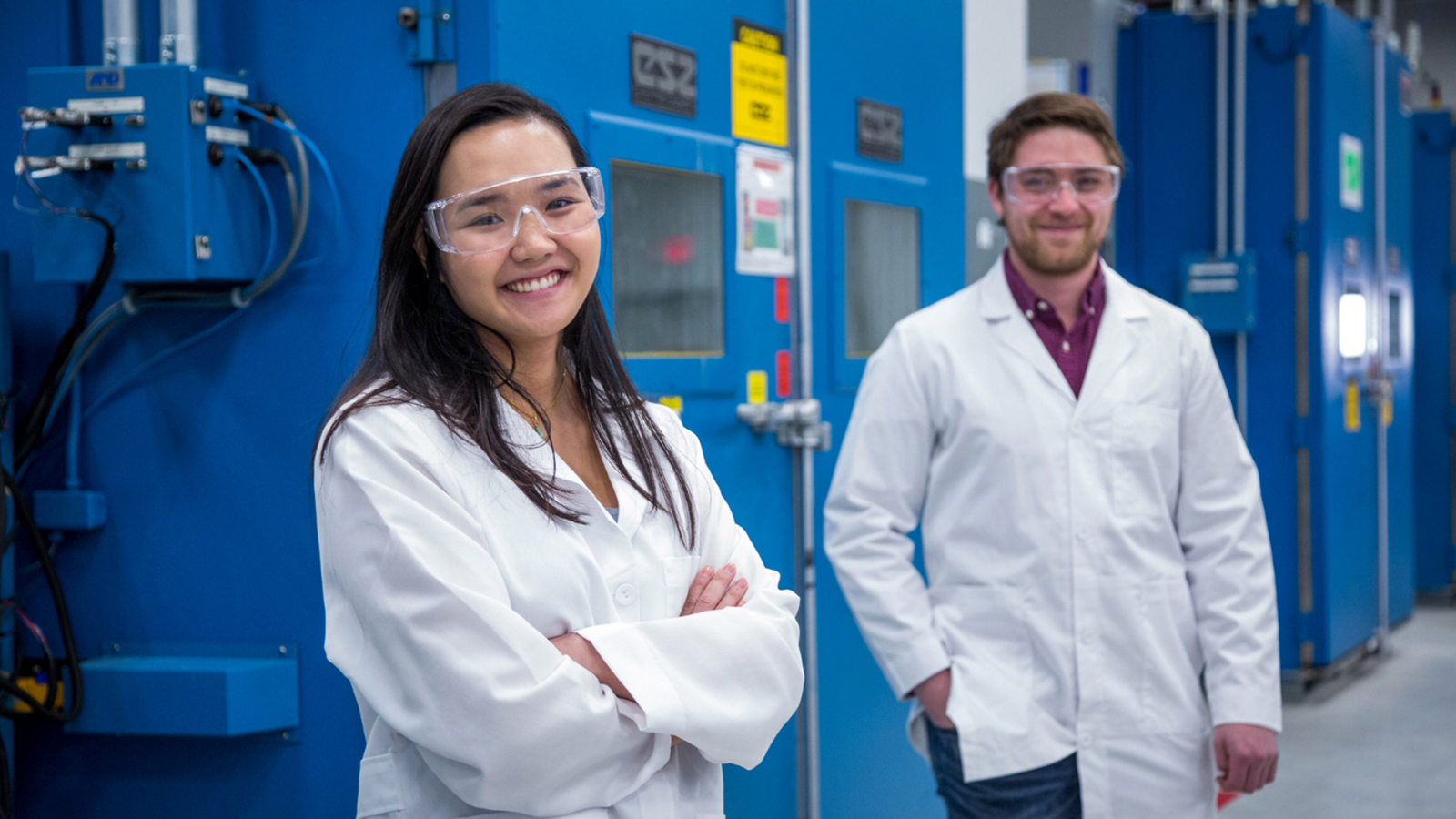 Woman and man in lab coat and safety glasses smiling