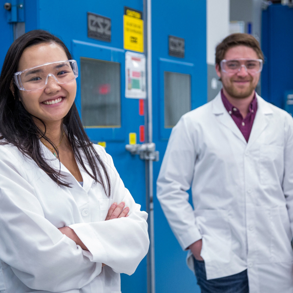 Woman and man in lab coat and safety glasses smiling