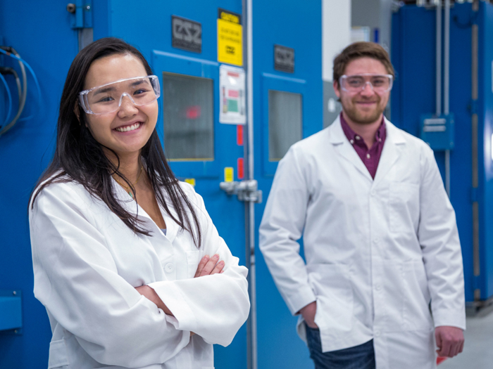 Woman and man in lab coat and safety glasses smiling