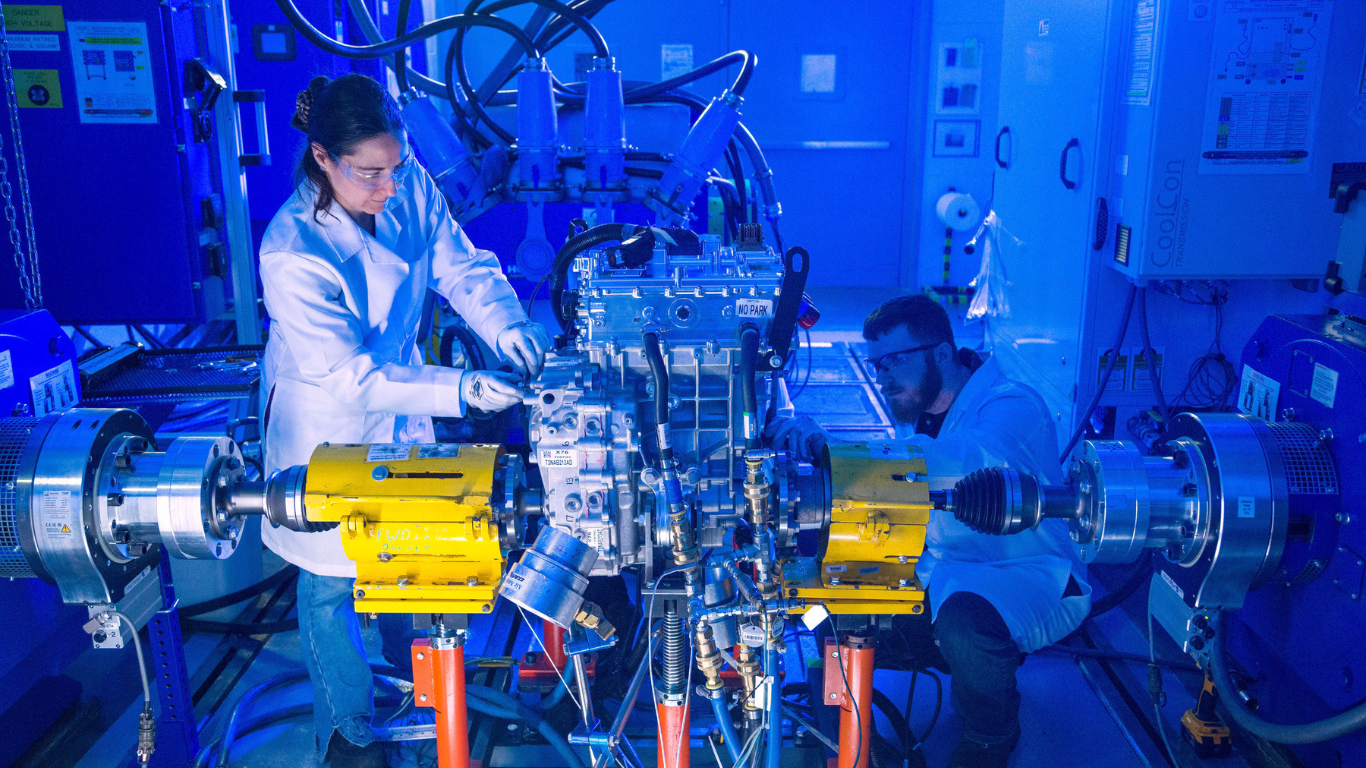 Workers in safety glasses and lab coats working technical machine
