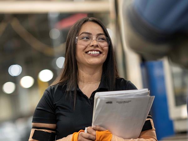Woman in safety glasses holding papers and smiling
