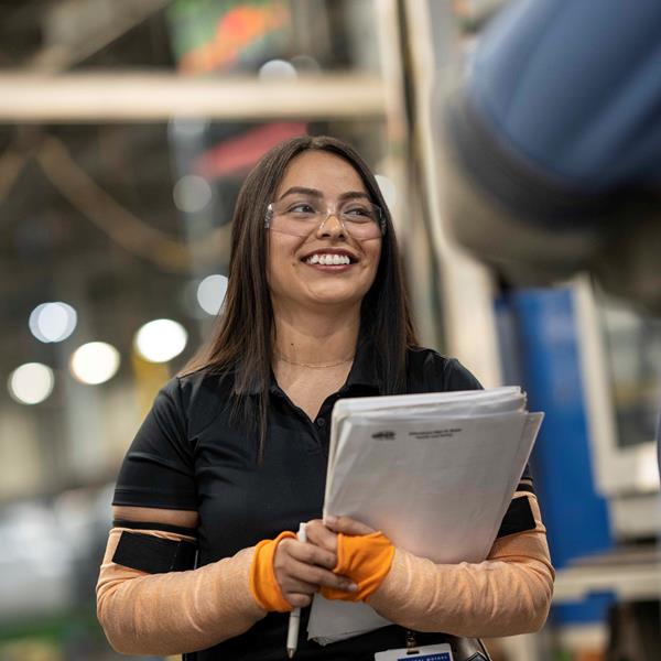 Woman in safety glasses holding papers and smiling